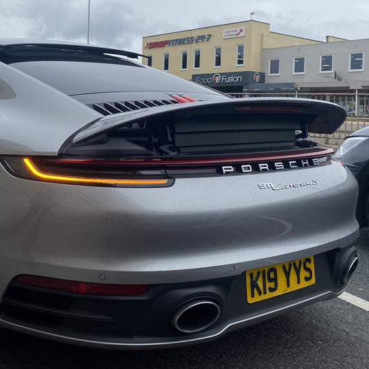 Back view of a Porsche car with a visible license plate in an urban setting.